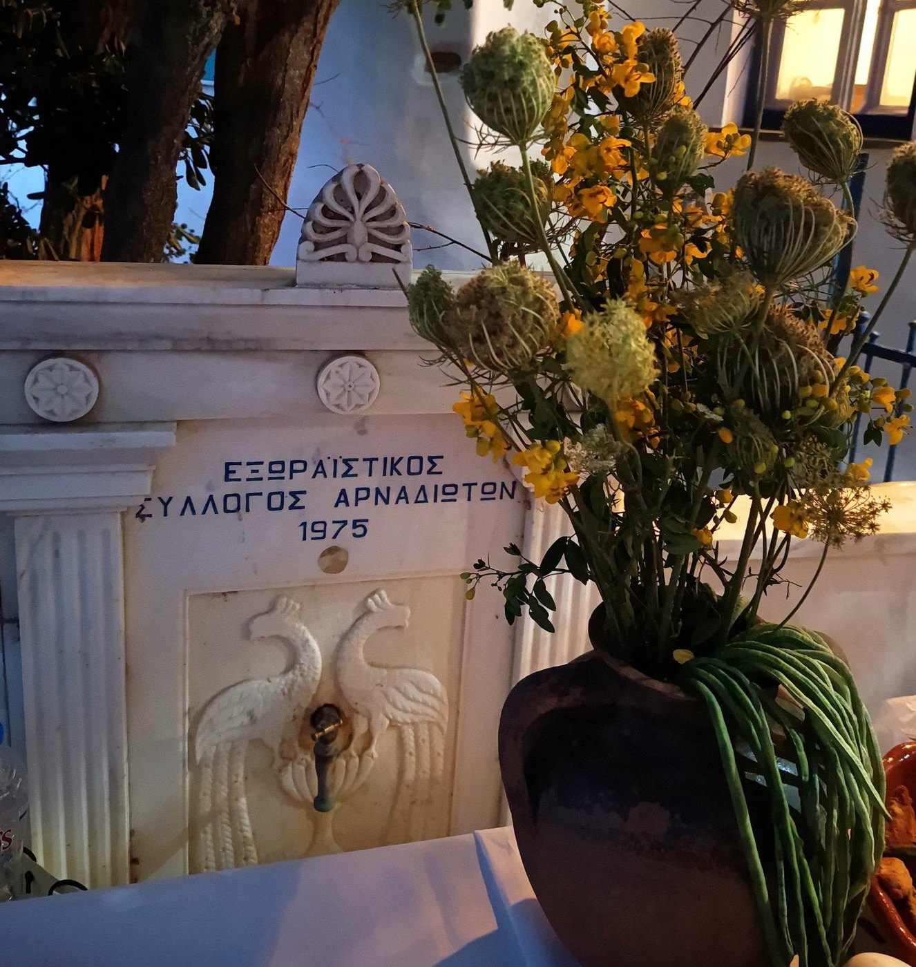 Μαρμάρινη κρήνη με ανάγλυφα πουλιά και την επιγραφή Εξωραϊστικός Σύλλογος Αρναδιωτών 1975