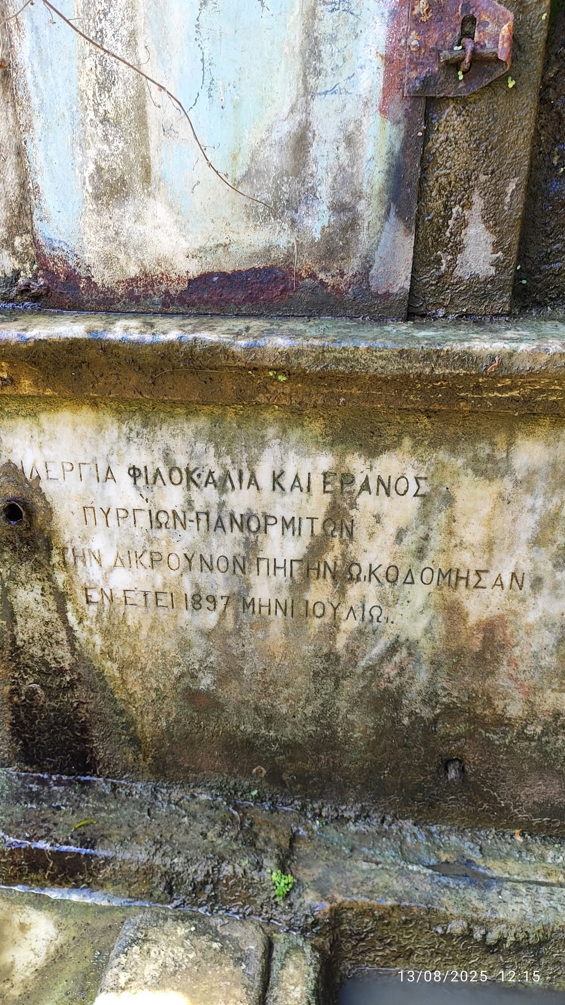 Μαρμάρινη επιγραφή του 1897 σε πηγή στη ρεματιά του Πύργου Τήνου, μαυρισμένη από τα βρύα