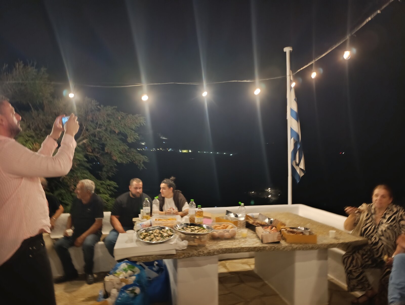 Το τραπέζι στην άκρη της αυλής, με τη σημαία και τη θάλασσα από κάτω