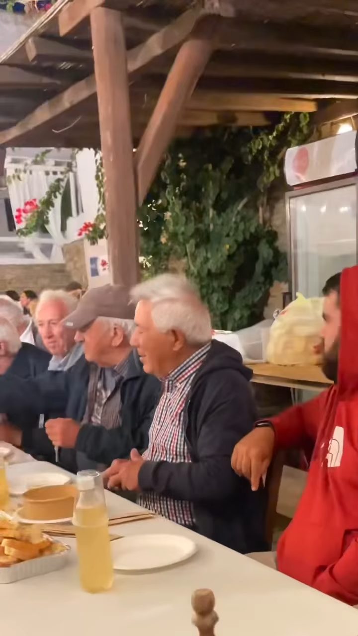 Χωριανοί και εθελοντές στο τραπέζι κάτω από την κληματαριά, μετά το πανηγύρι του Κάμπου Τήνου