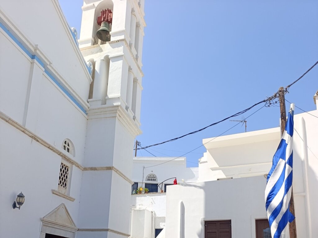 Το καμπαναριό της καθολικής εκκλησίας της Κώμης Τήνου με την ελληνική σημαία την ημέρα της πανήγυρης του Αγίου Ιωάννη