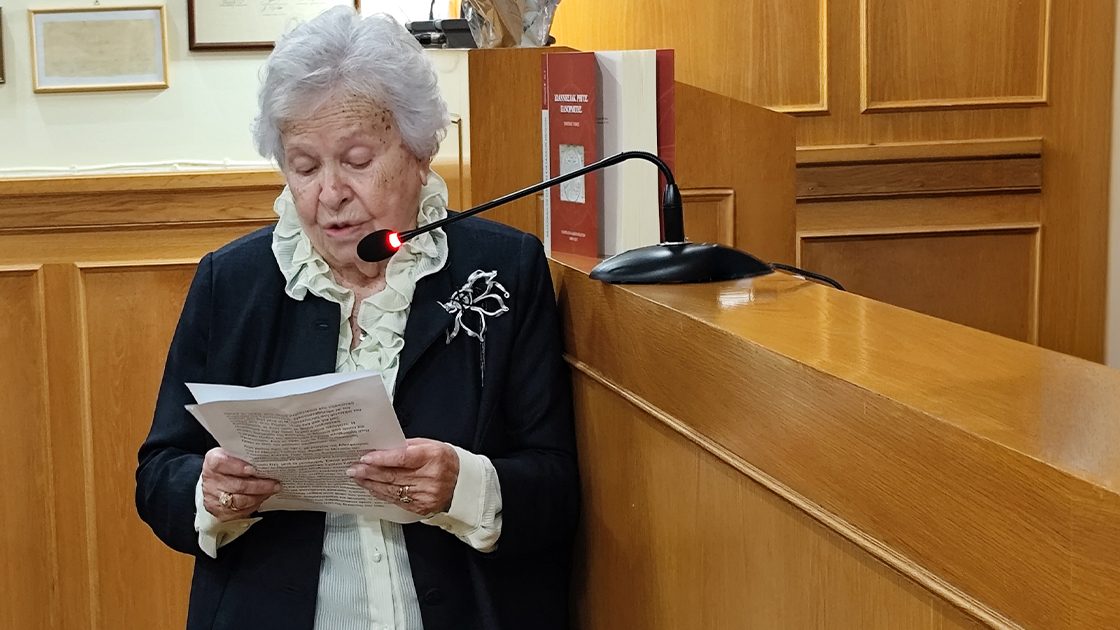 Η Μαίρη Βορρέ-Γαΐτη διαβάζει κείμενο σε αναλόγιο, σε αίθουσα με ξύλινη επένδυση