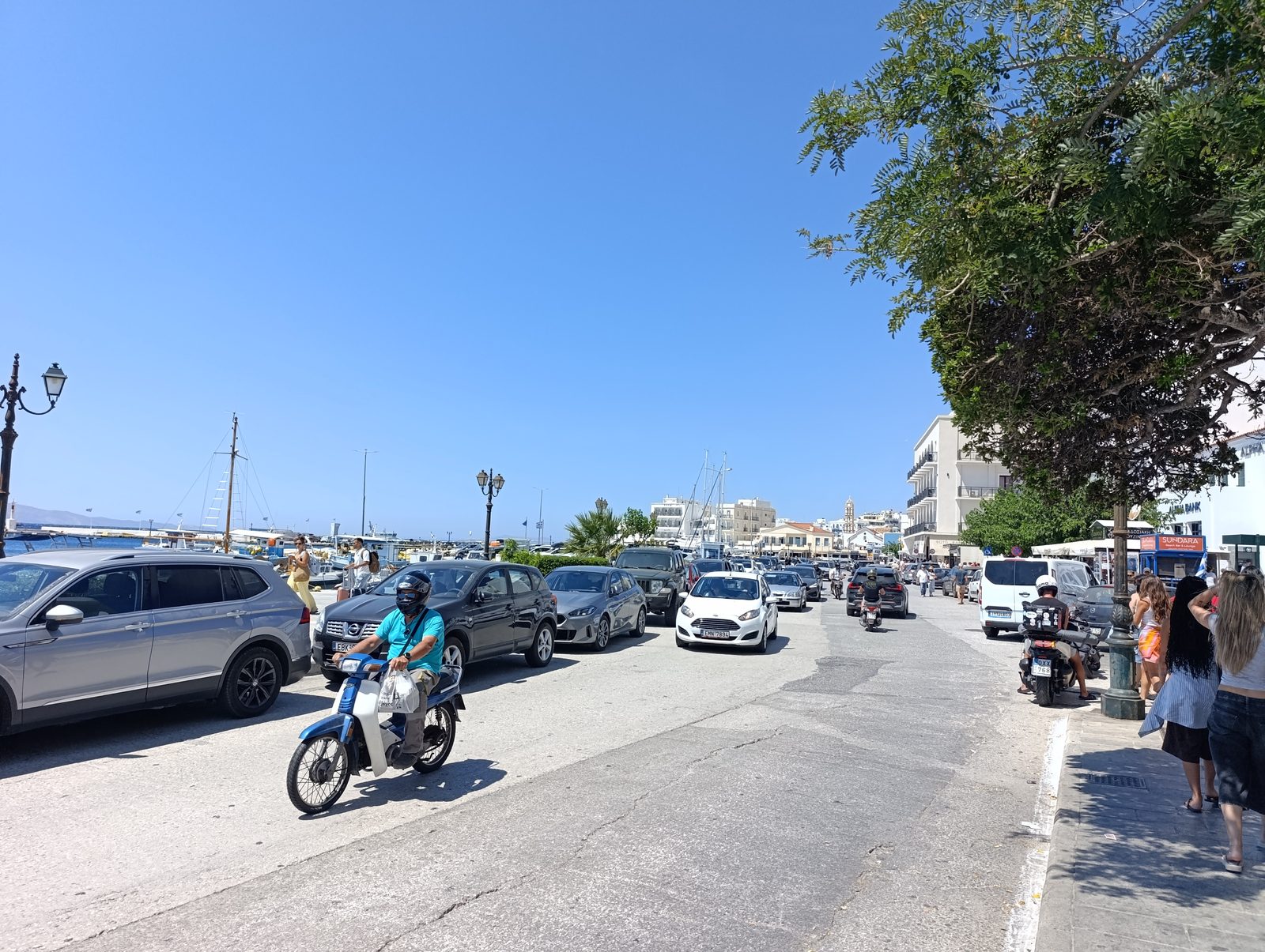 Κίνηση οχημάτων και πεζών στην παραλιακή της Τήνου το μεσημέρι
