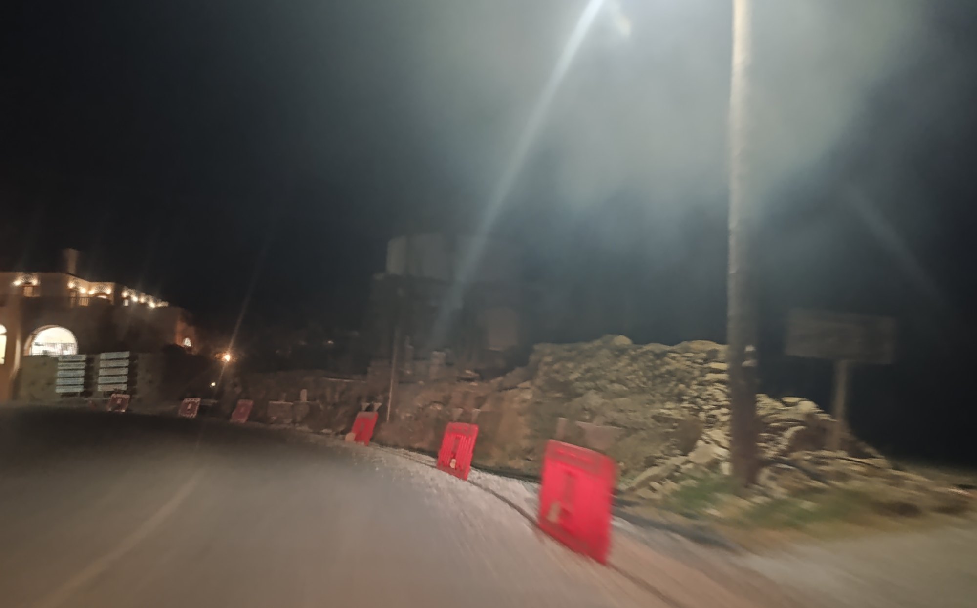 Σειρά από κόκκινα πλαστικά κιγκλιδώματα στη δεξιά πλευρά του δρόμου, μπροστά από ξερολιθιά και τον ανεμόμυλο, τη νύχτα
