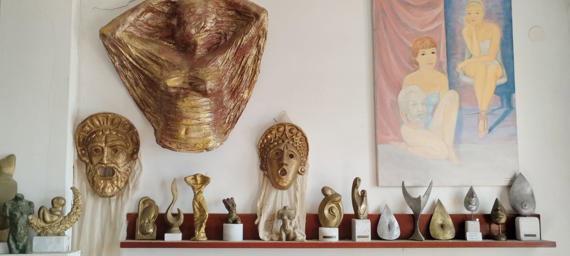 Χρυσές θεατρικές μάσκες και μικρογλυπτά σε μέταλλο πάνω σε ράφι