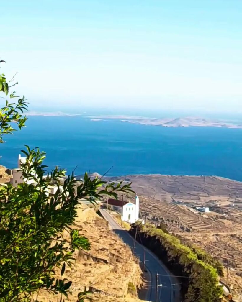 Άσπρο εκκλησάκι δίπλα στον δρόμο στον Αρνάδο Τήνου, με τη Δήλο και τη Ρήνεια απέναντι