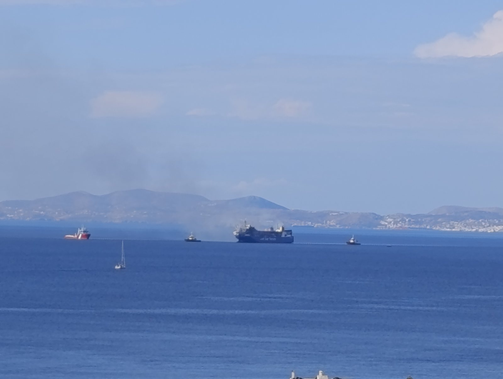 Το BLUE CARRIER 2 με καπνό, ρυμουλκά και σκάφη αρωγής, από τη Χώρα της Τήνου το πρωί του Σαββάτου 26 Σεπτεμβρίου 2026