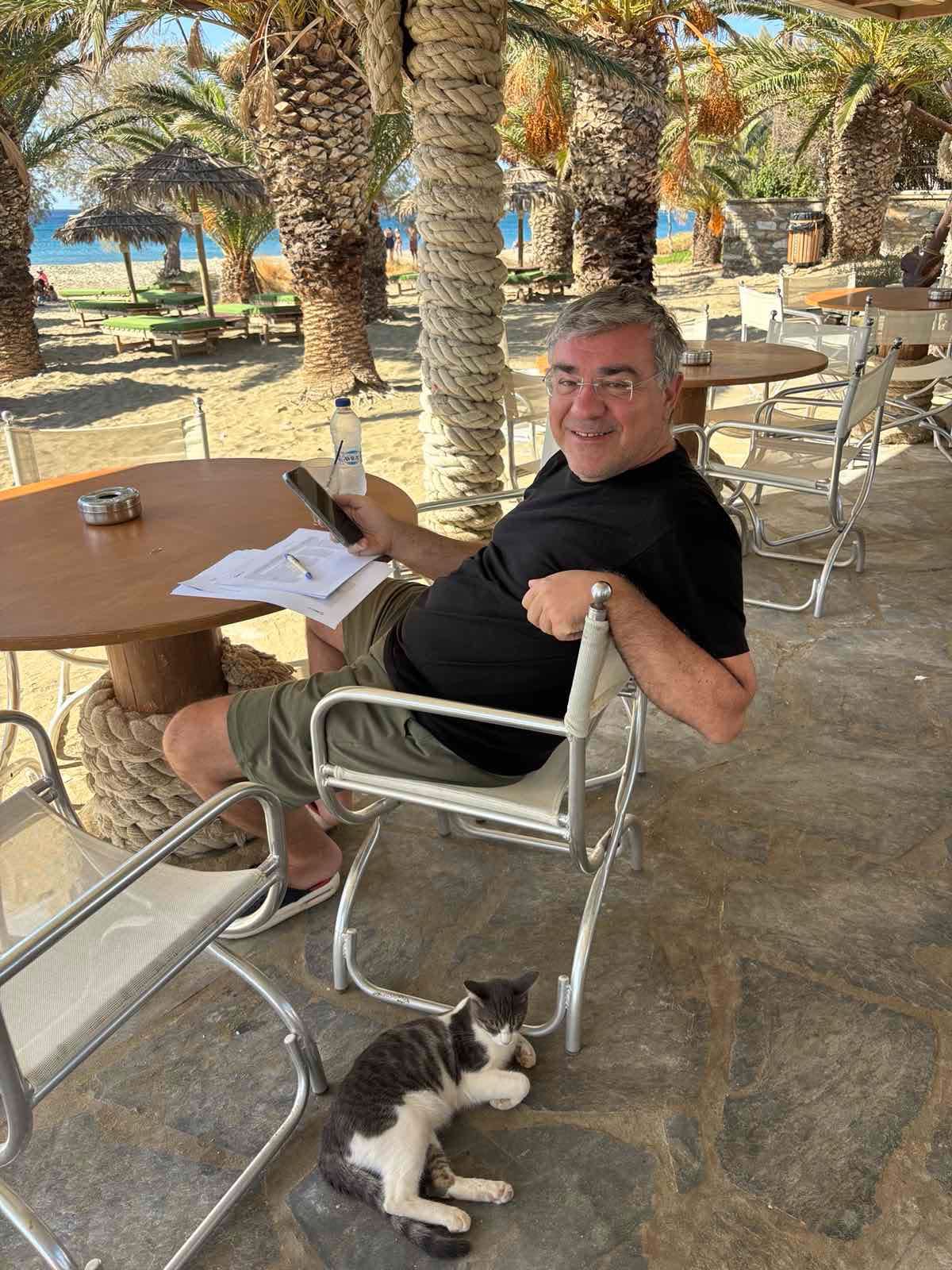 Ο Μανώλης Γραφάκος σε beach bar της Τήνου με μια γάτα στα πόδια του