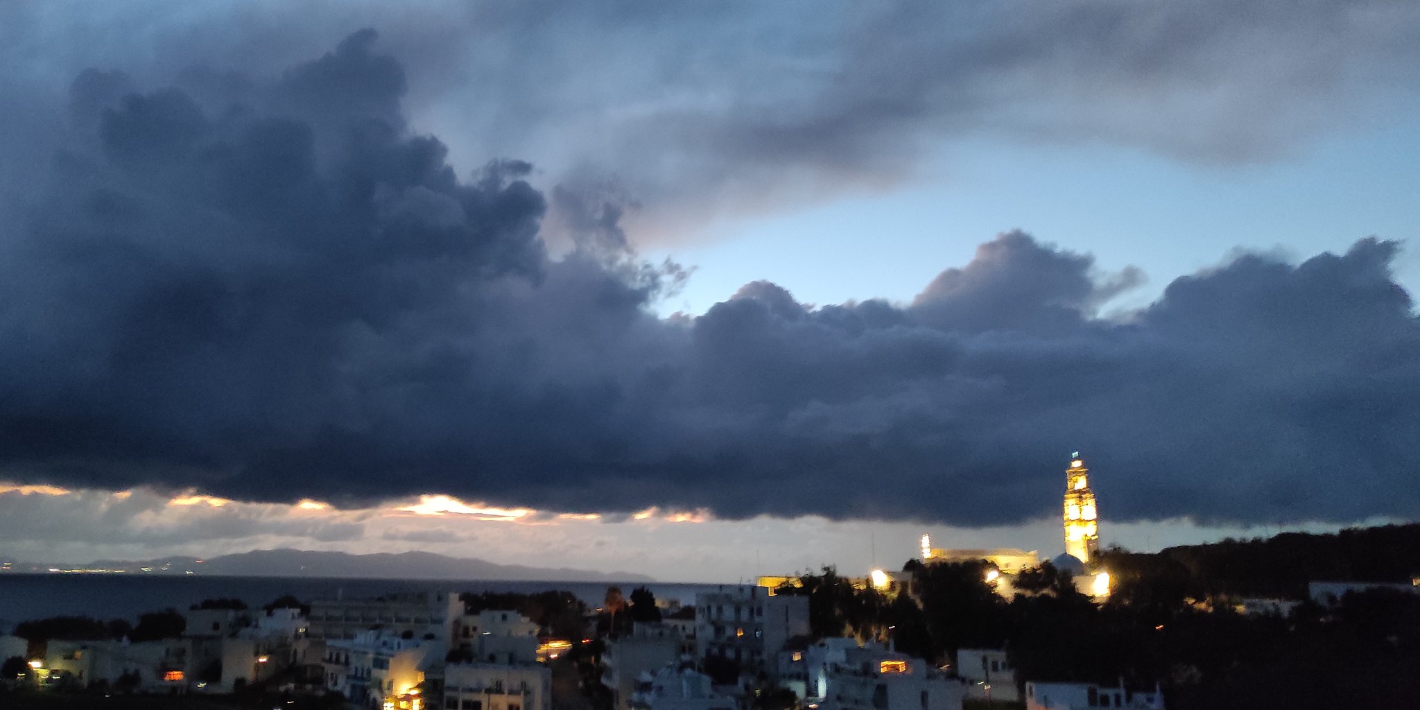 Σύννεφα βροχής πάνω από τη Χώρα της Τήνου, με φωτισμένο το καμπαναριό της Ευαγγελίστριας