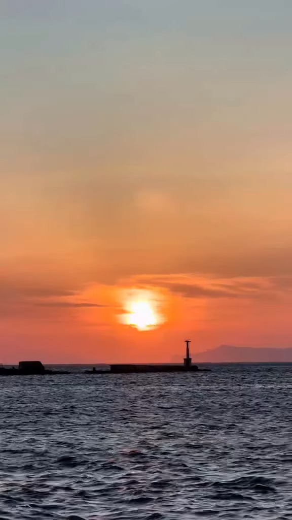 Ηλιοβασίλεμα πάνω από τον φάρο του λιμανιού της Τήνου — στιγμιότυπο από το βίντεο του Νίκου Καμολίνου