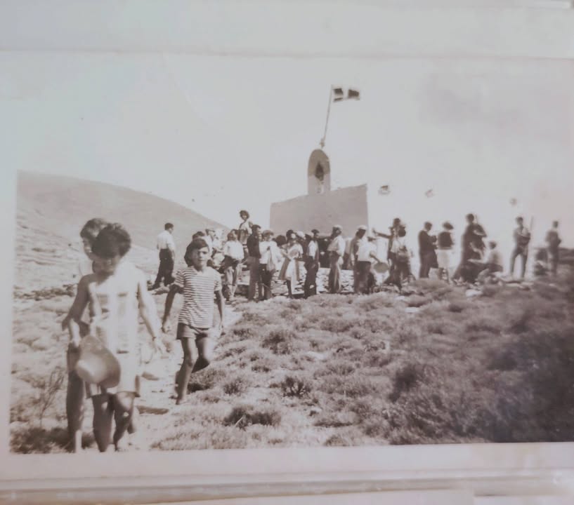 Παλιά φωτογραφία: κόσμος μαζεμένος σε ξωκλήσι με υψωμένη σημαία