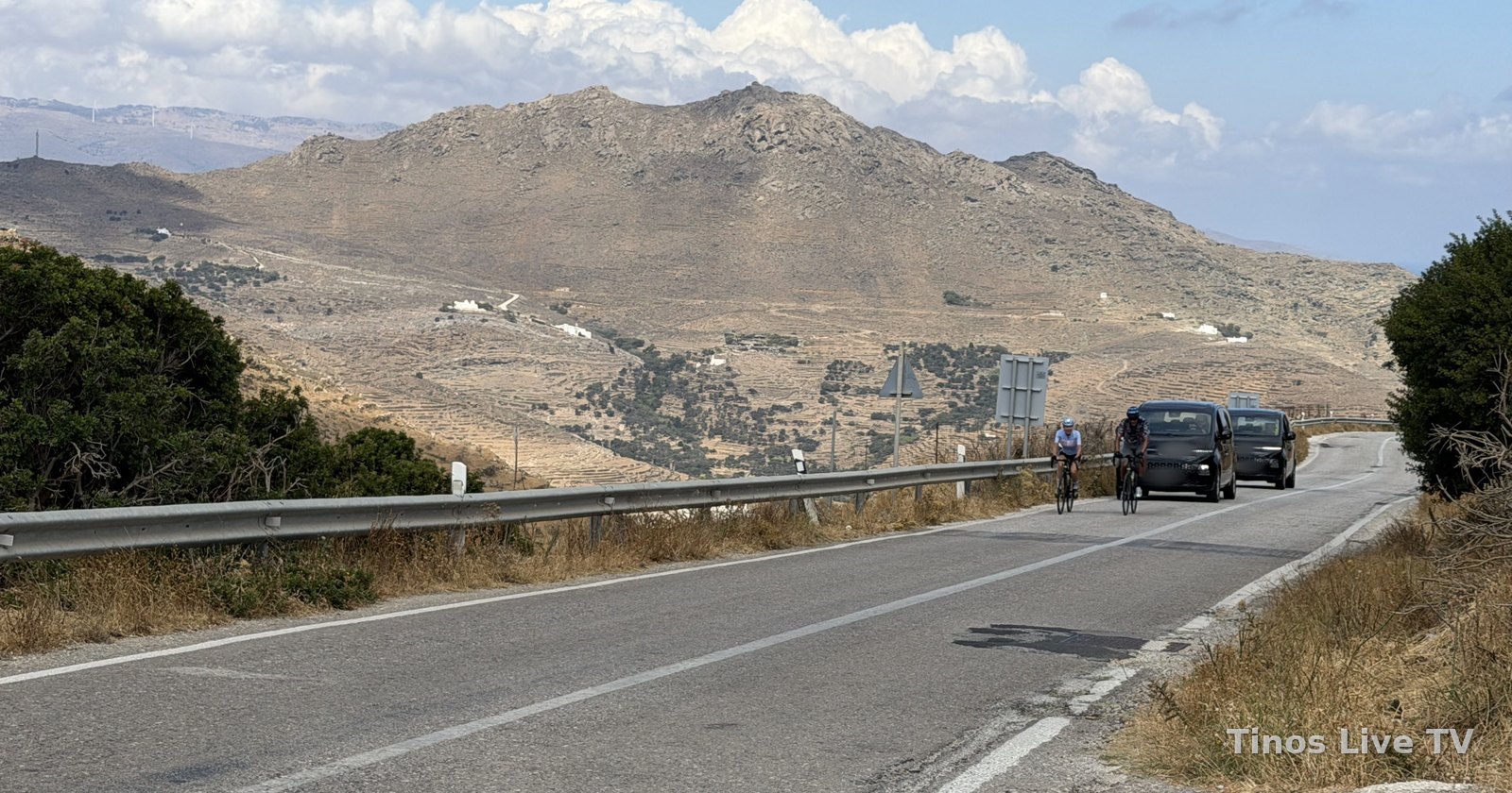 Δύο ποδηλάτες σε δρόμο της Τήνου με τα συνοδευτικά οχήματα πίσω τους