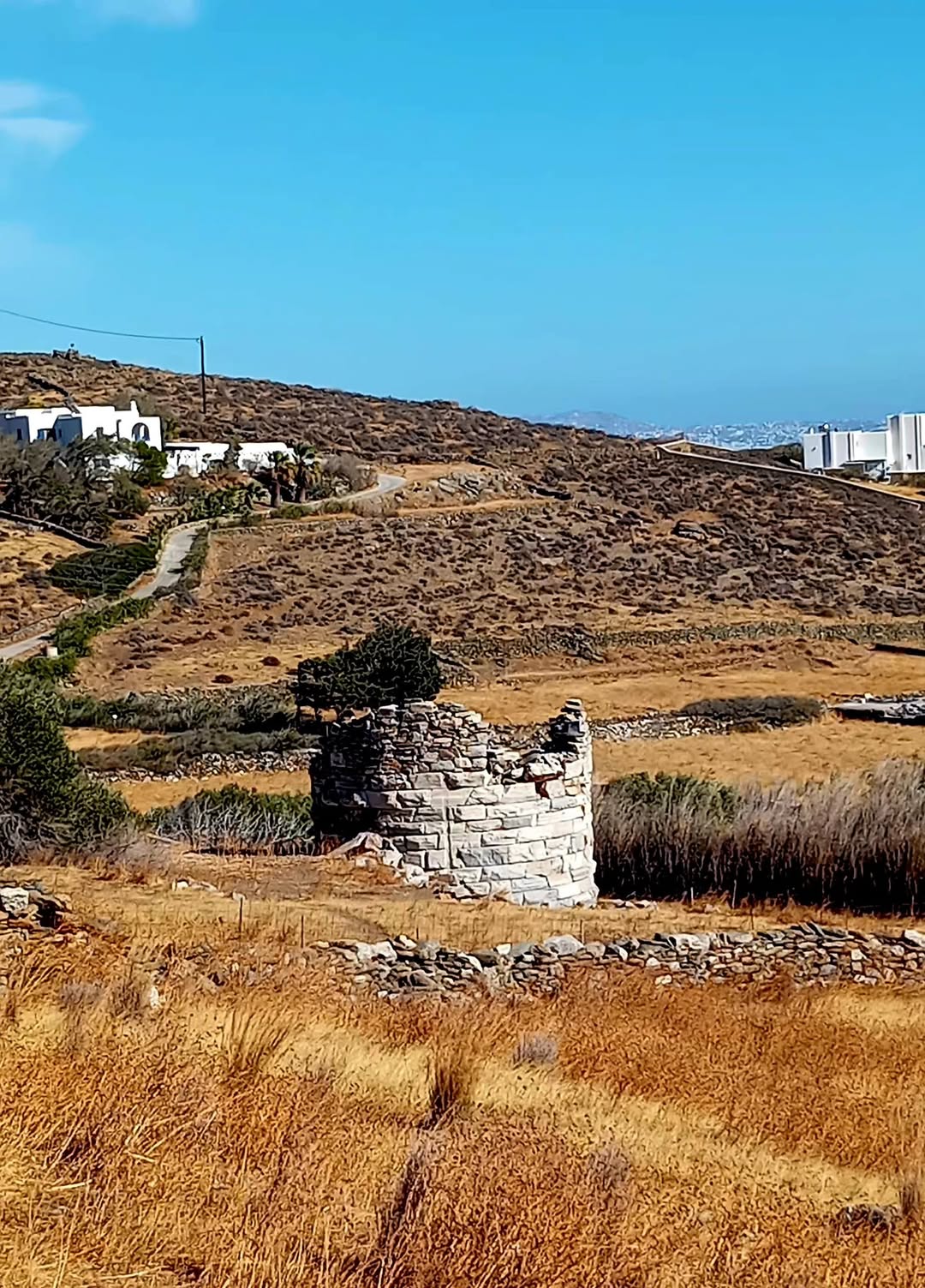 Ο κυκλικός μαρμάρινος πύργος στο Σμόβολο της Τήνου, μέσα σε ξερό λιβάδι με ξερολιθιές
