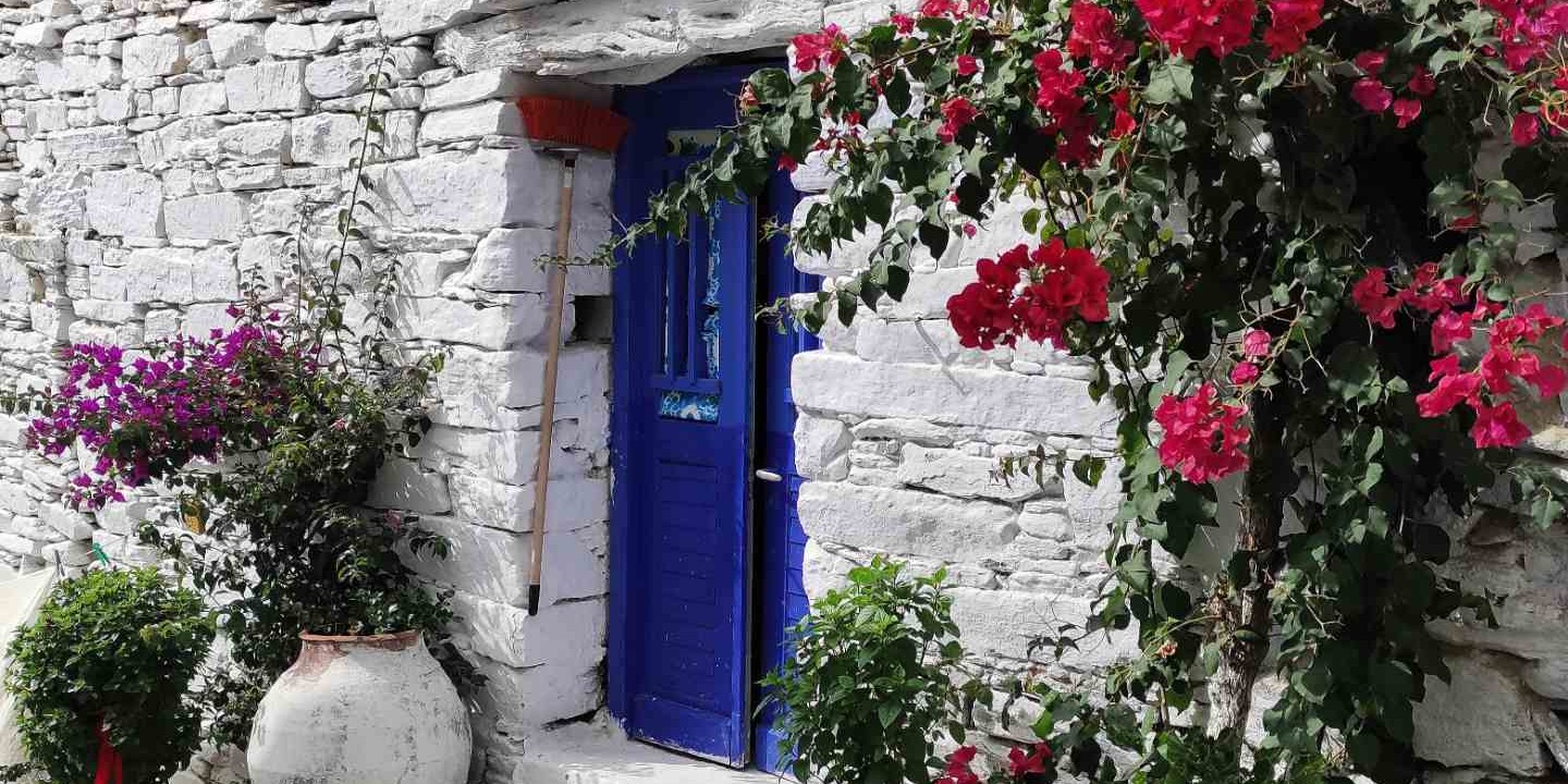 Μπλε πόρτα με βουκαμβίλιες σε ξερολιθικό σπίτι χωριού της Τήνου