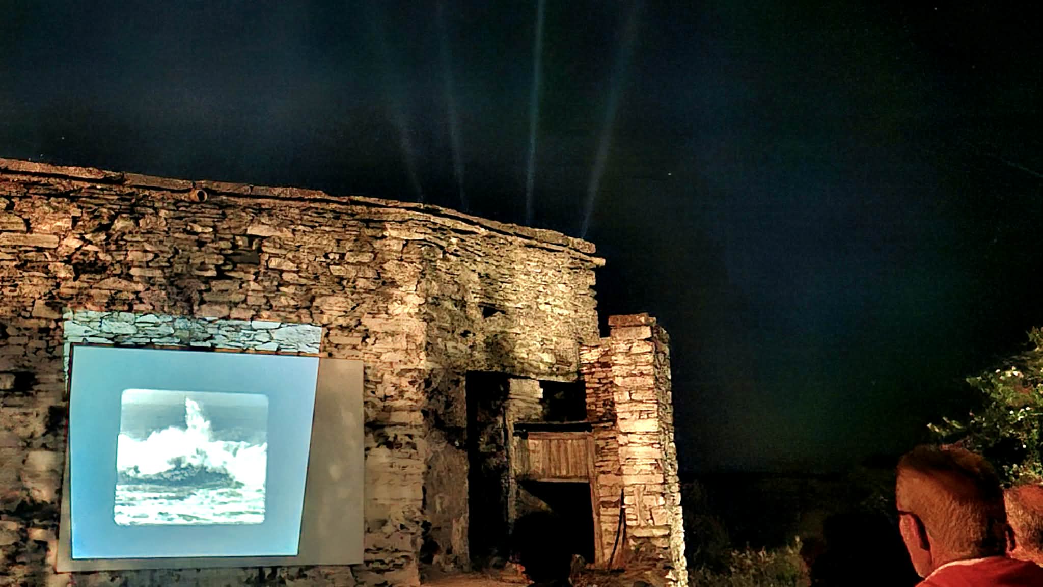 Η οθόνη πάνω στην ξερολιθιά, με τη δέσμη του προβολέα στον νυχτερινό ουρανό