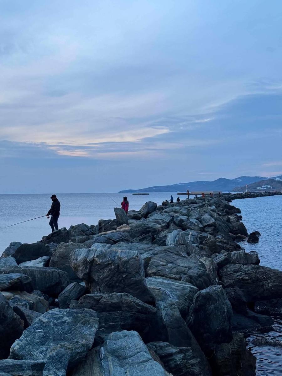 Ψαράδες με καλάμια στον πέτρινο λιμενοβραχίονα του λιμένα Τήνου το σούρουπο