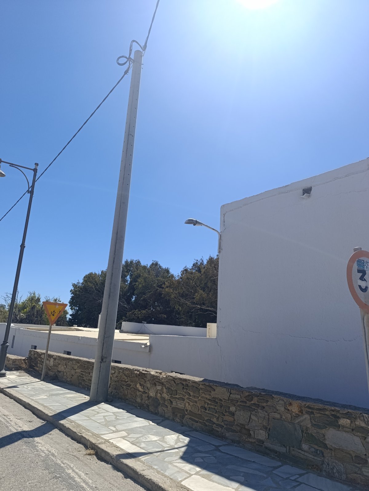 Τσιμεντένια κολόνα σε πλακόστρωτο πεζοδρόμιο δίπλα σε πέτρινο τοιχίο