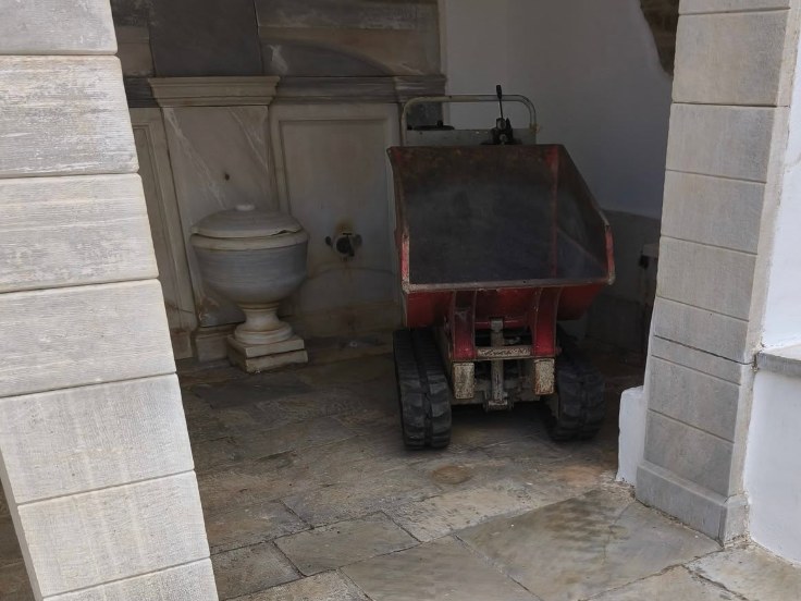 Ερπυστριοφόρο μηχάνημα μεταφοράς υλικών σταθμευμένο μέσα στο ανακαινισμένο Πηγάδι στα Πλατιά της Τήνου, δίπλα στη μαρμάρινη κρήνη