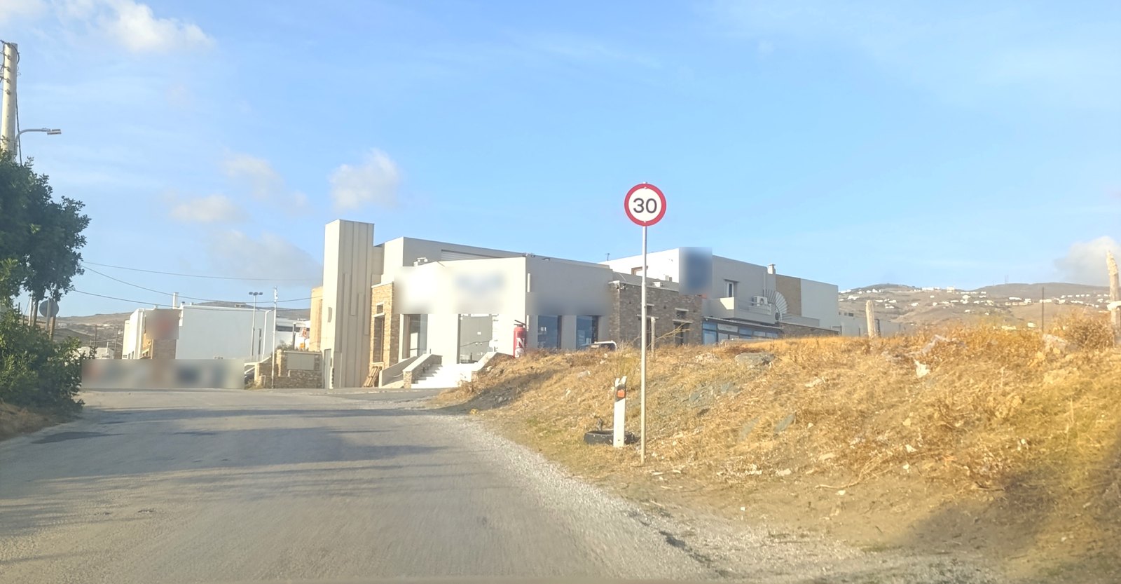 Πινακίδα ορίου ταχύτητας 30 χλμ./ώρα στη Λεωφόρο Τριποτάμου στην Τήνο, λίγο πριν από τα καταστήματα