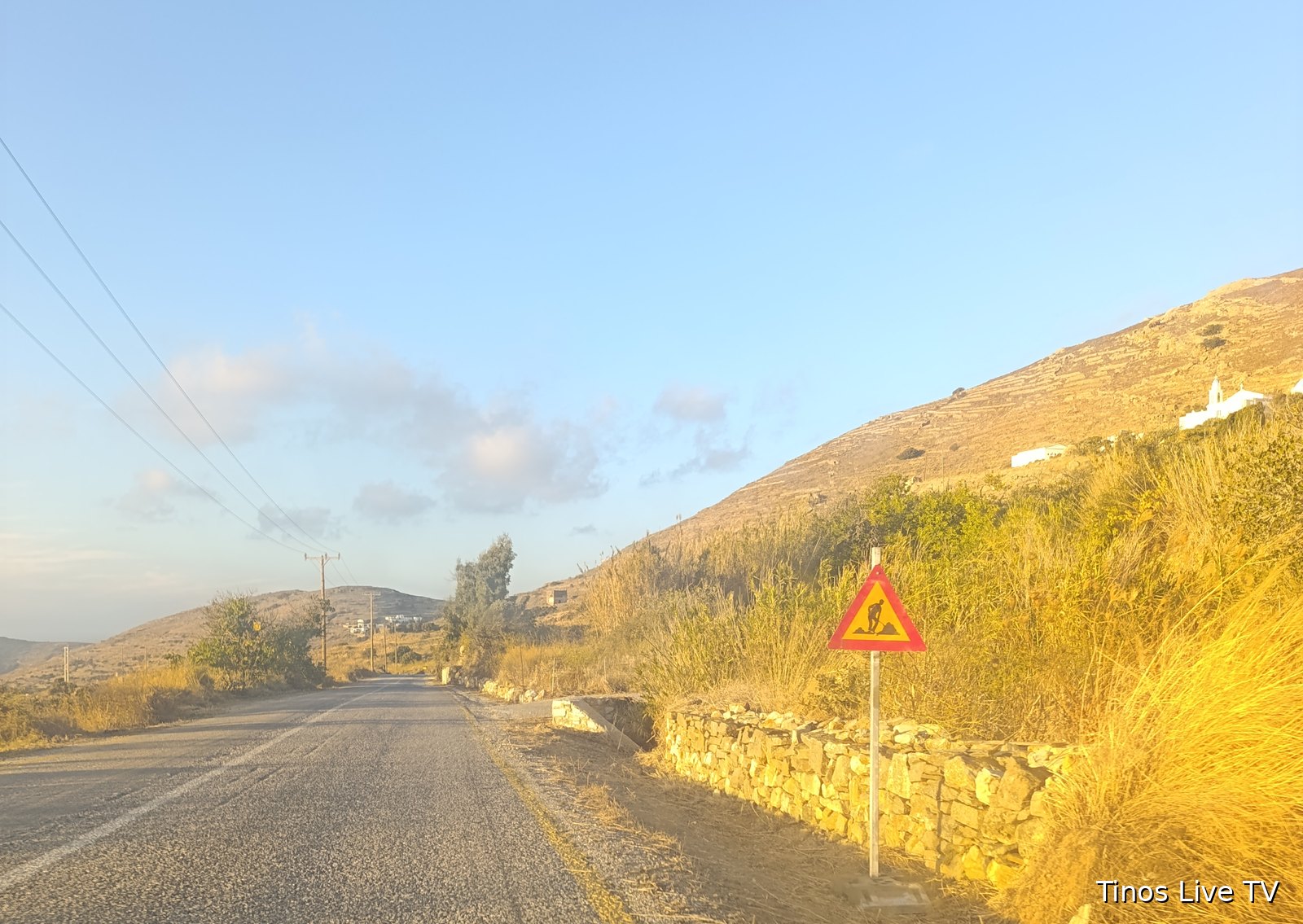 Τριγωνική πινακίδα «Εκτελούνται εργασίες στην οδό» δίπλα σε ξερολιθιά, στον δρόμο Ξυνάρας – Λουτρών στην Τήνο