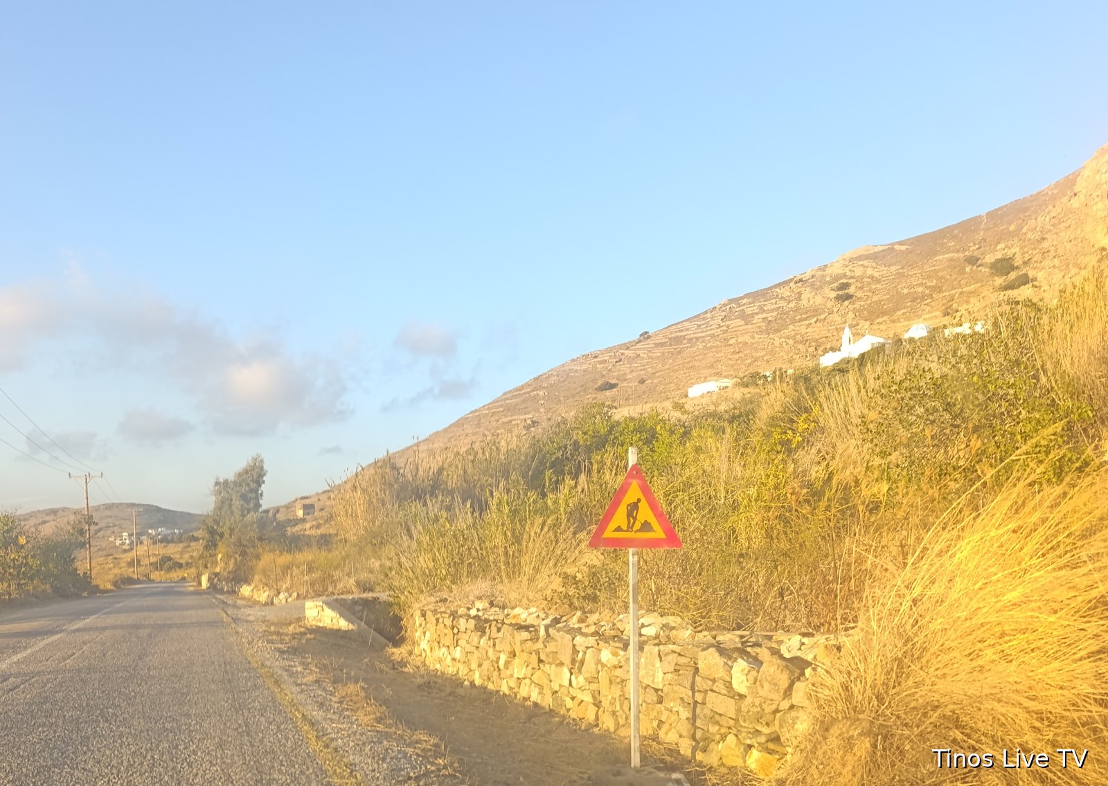 Πινακίδα «Εκτελούνται εργασίες στην οδό» μπροστά σε ξερολιθιά και καθαρισμένη τάφρο στον δρόμο προς τα Λουτρά Τήνου