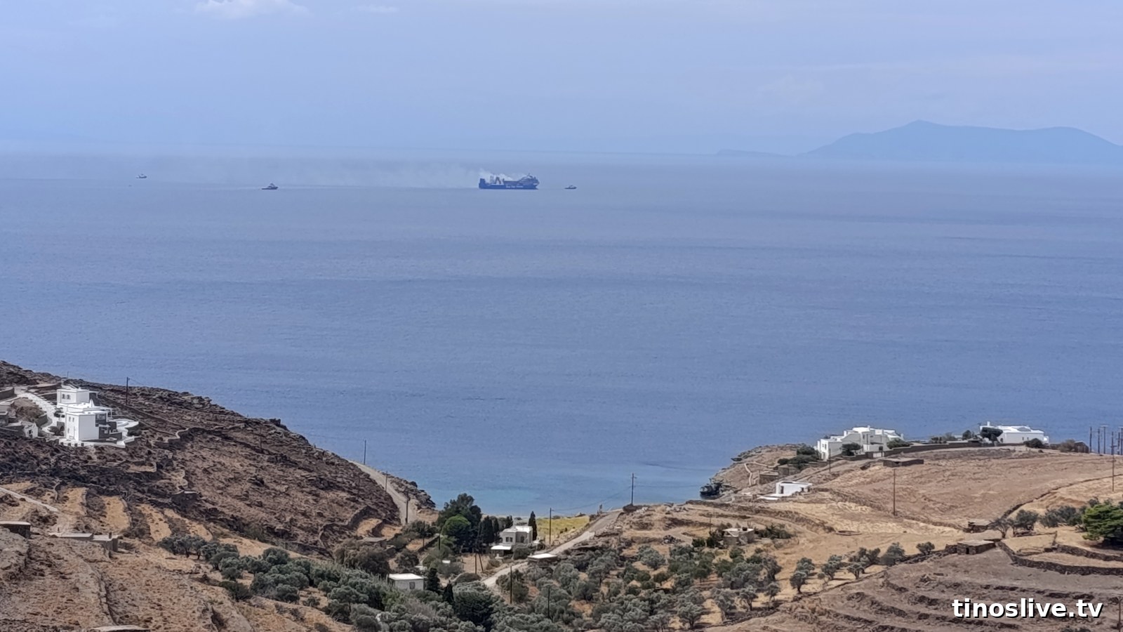 Το BLUE CARRIER 2 με καπνό και τα ρυμουλκά ανοιχτά του Αγίου Ρωμανού Τήνου, από την Πανούσα