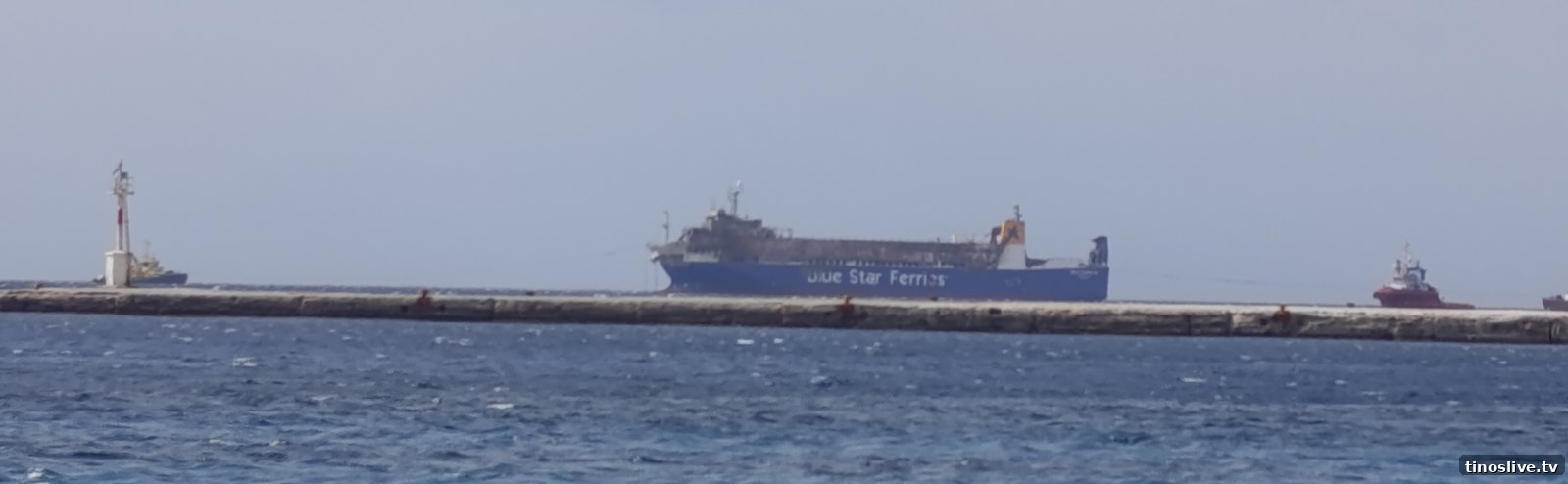 Το BLUE CARRIER 2 με τα ρυμουλκά, όπως φαίνεται πίσω από τον κυματοθραύστη του λιμανιού της Τήνου, 3 Οκτωβρίου 2026