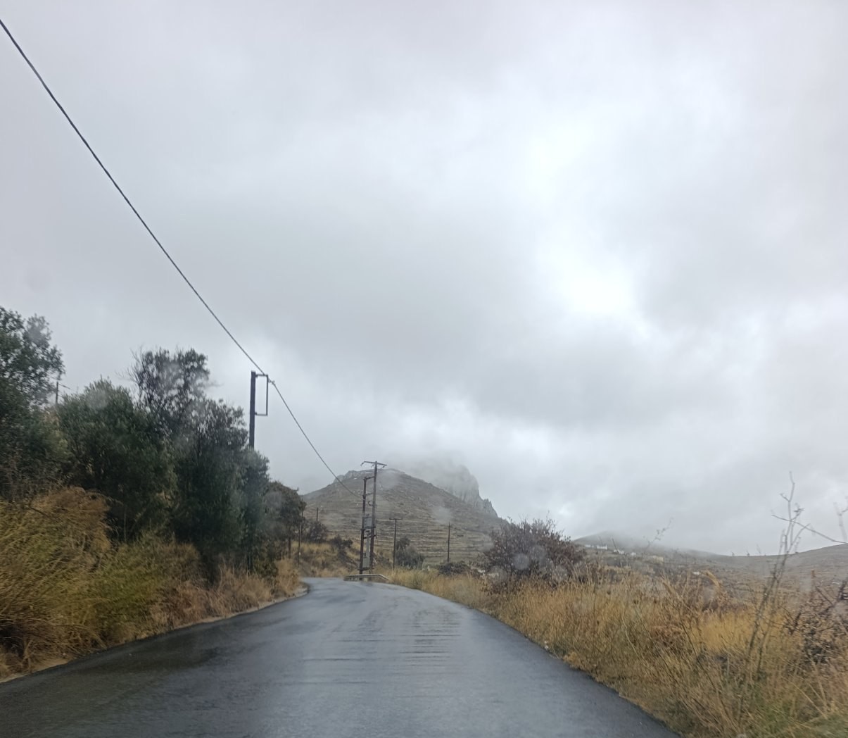 Βρεγμένος επαρχιακός δρόμος από το παρμπρίζ αυτοκινήτου, με σύννεφα πάνω από τον λόφο