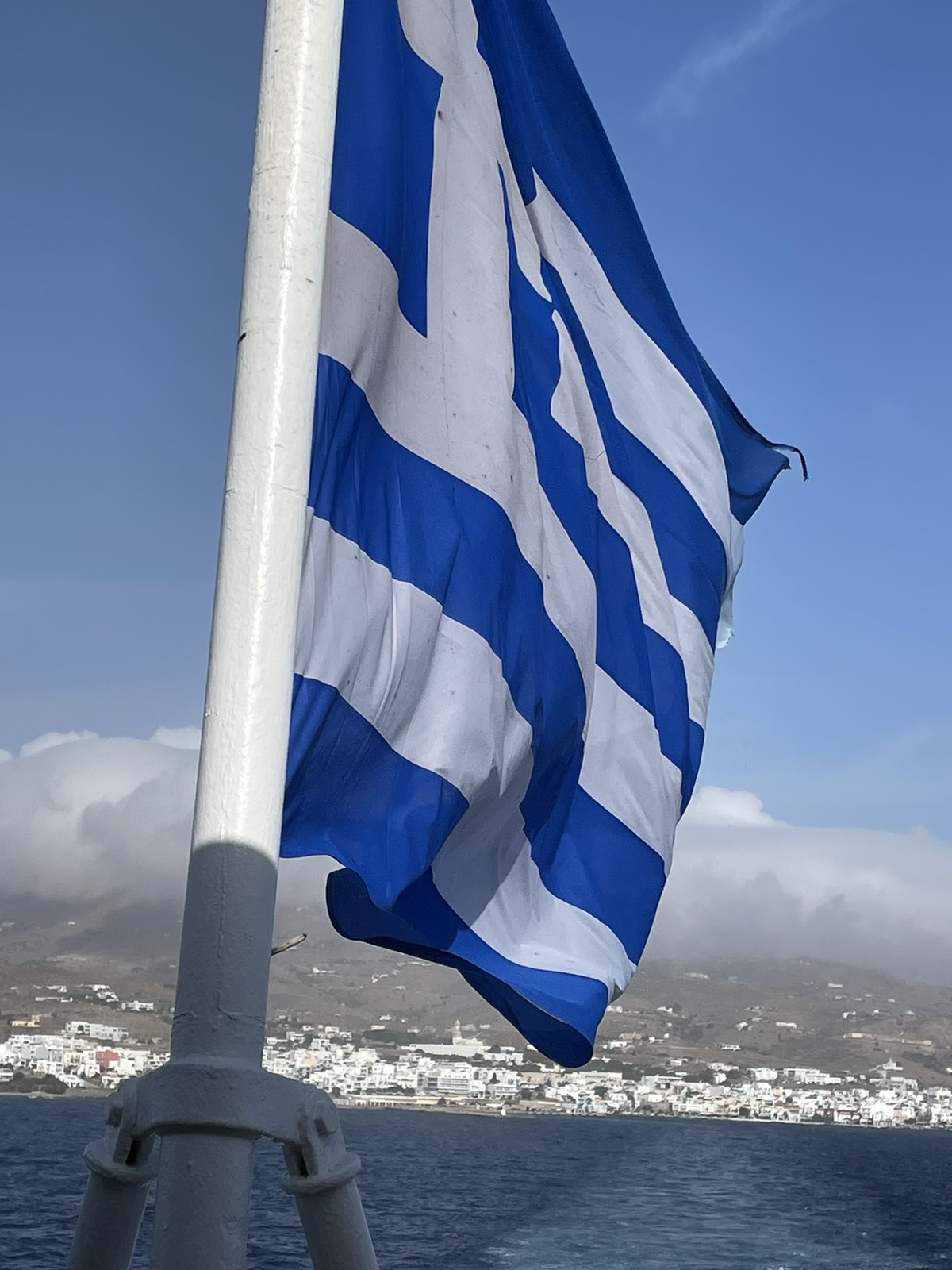 Η ελληνική σημαία σε πλοίο, με τη Χώρα και το λιμάνι της Τήνου πίσω