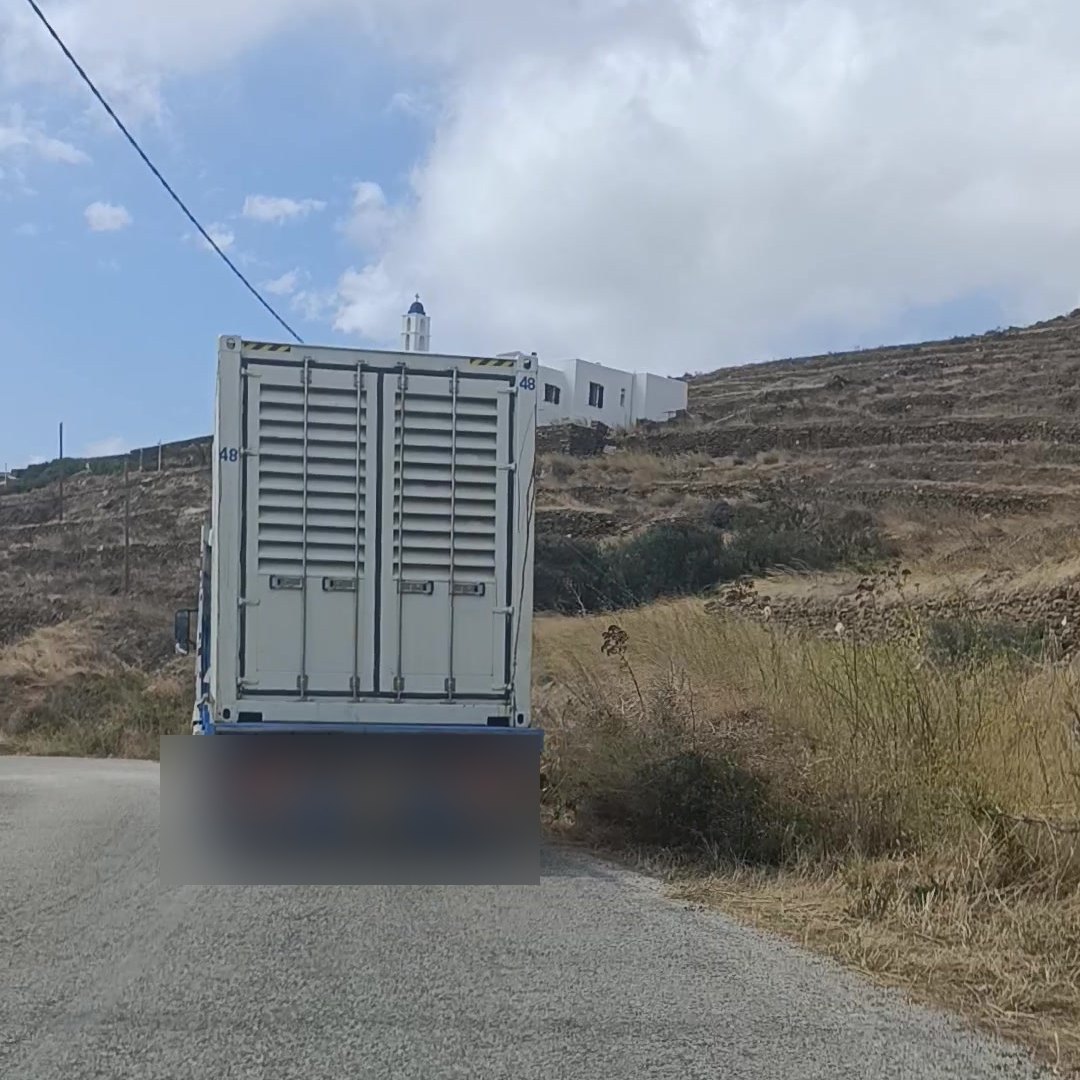 Φορτηγό με κοντέινερ-γεννήτρια περνά δίπλα από οικισμό της Τήνου, 1 Οκτωβρίου 2026