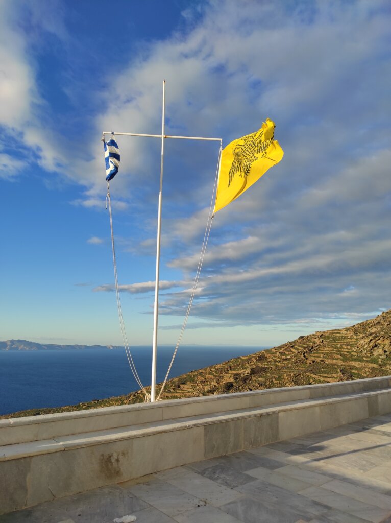 Η ελληνική σημαία δίπλα στη βυζαντινή σημαία, πάνω από τις πεζούλες και τη θάλασσα της Τήνου