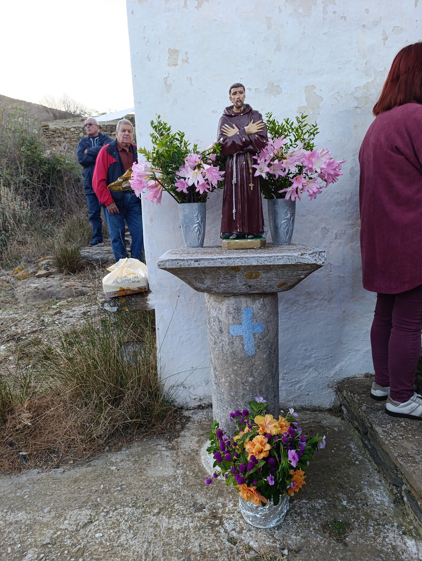 Αγαλματάκι του Αγίου Φραγκίσκου με λουλούδια σε πέτρινη κολόνα έξω από το εκκλησάκι