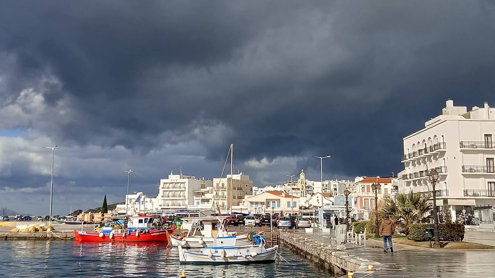 Βαριά σκούρα σύννεφα πάνω από το λιμάνι της Τήνου, με καΐκια και βρεγμένο μαρμάρινο μόλο