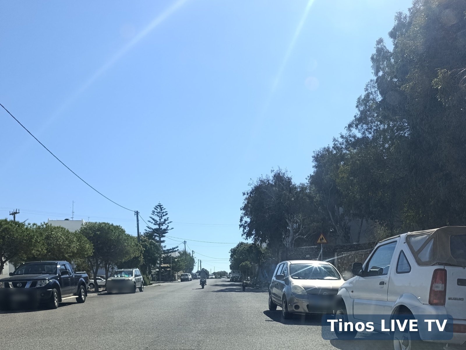 Η πινακίδα «Προσοχή, παιδιά» στον δρόμο του 3ου Δημοτικού Τήνου, με σταθμευμένα αυτοκίνητα και ελεύθερο οδόστρωμα