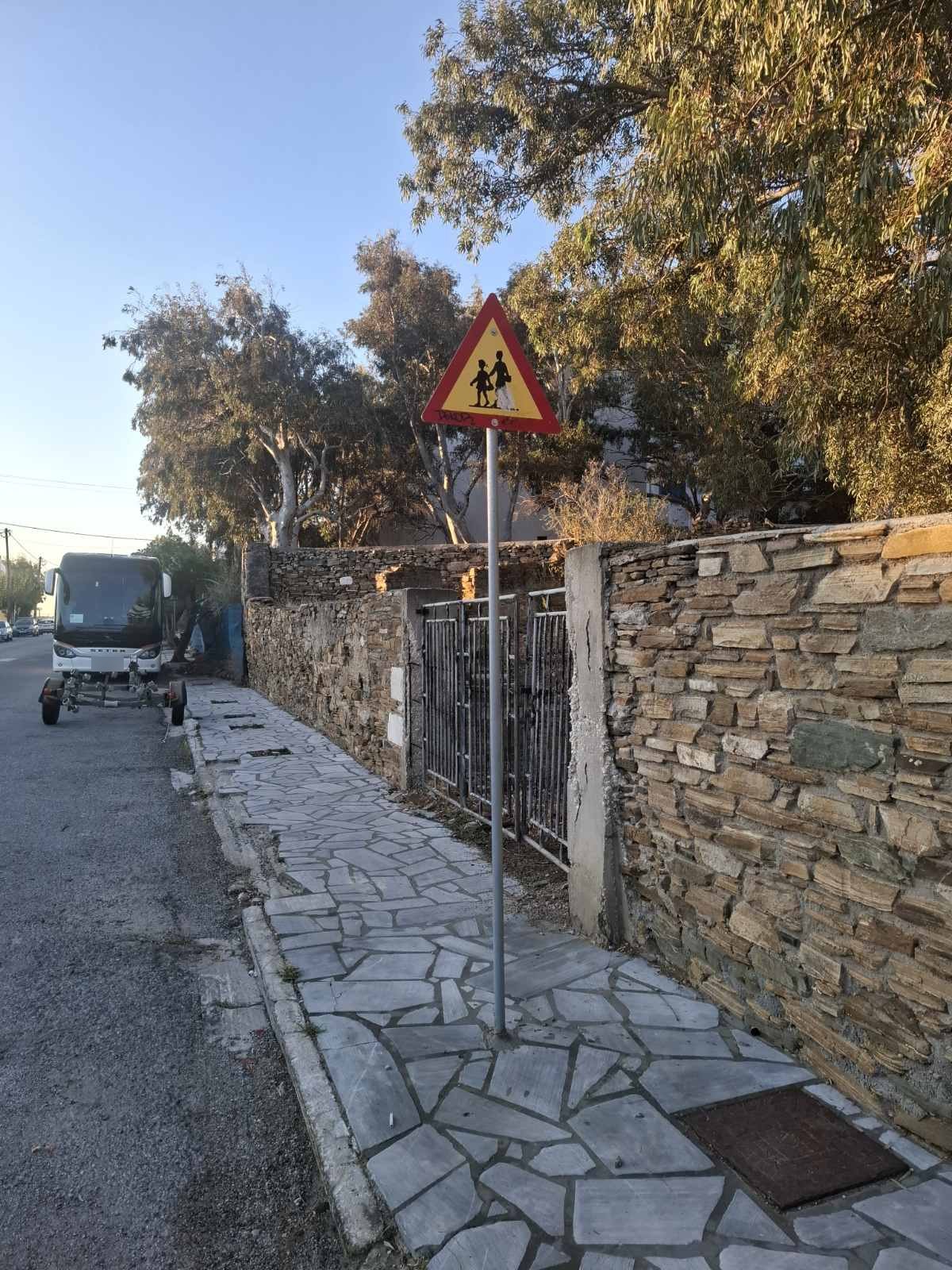 Τριγωνική πινακίδα «Προσοχή, παιδιά» στο πεζοδρόμιο, με το πούλμαν σταθμευμένο πιο κάτω
