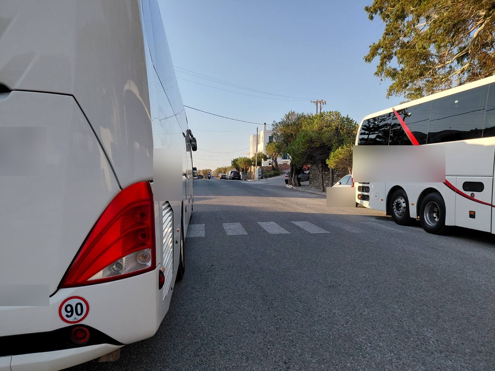 Τουριστικά πούλμαν σταθμευμένα δεξιά και αριστερά της διάβασης πεζών στον δρόμο για το 3ο Δημοτικό Τήνου