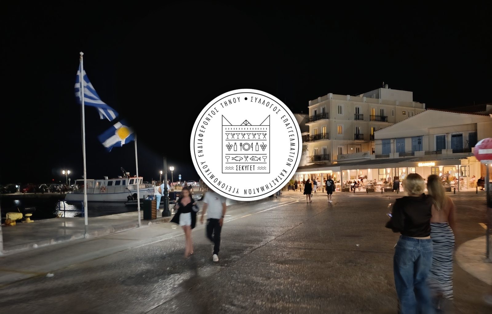 Το σήμα του Συλλόγου Επαγγελματιών Καταστημάτων Υγειονομικού Ενδιαφέροντος Τήνου (ΣΕΚΥΓΕΤ) πάνω από το λιμάνι της Τήνου τη νύχτα