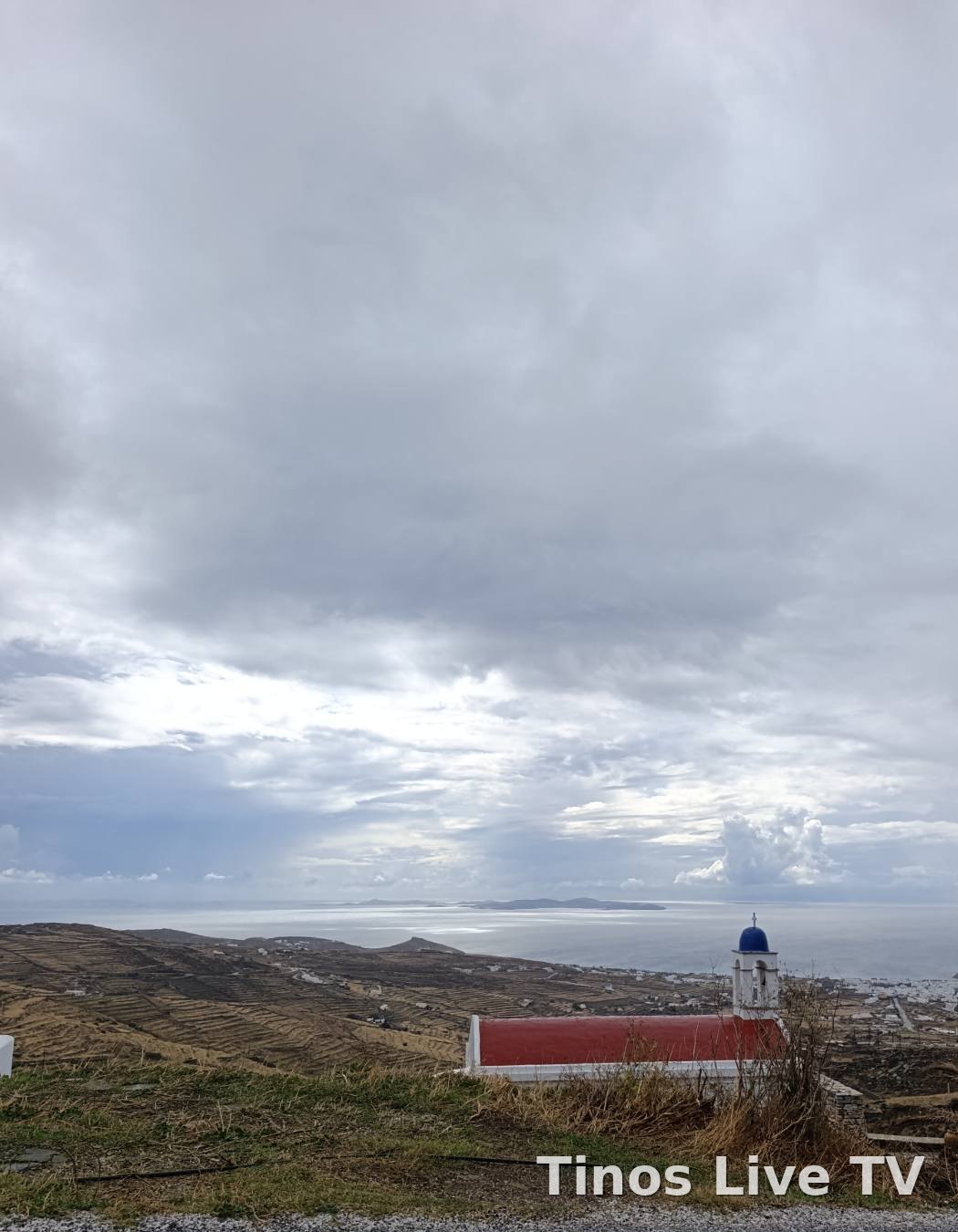 Βαριά σύννεφα πάνω από τη Χώρα και το λιμάνι της Τήνου, με εκκλησάκι σε πρώτο πλάνο