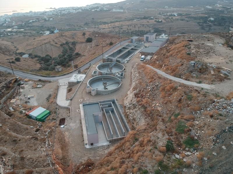 Αεροφωτογραφία της Εγκατάστασης Επεξεργασίας Λυμάτων της Τήνου ψηλά στην πλαγιά, με την πόλη και το λιμάνι της Τήνου στο βάθος
