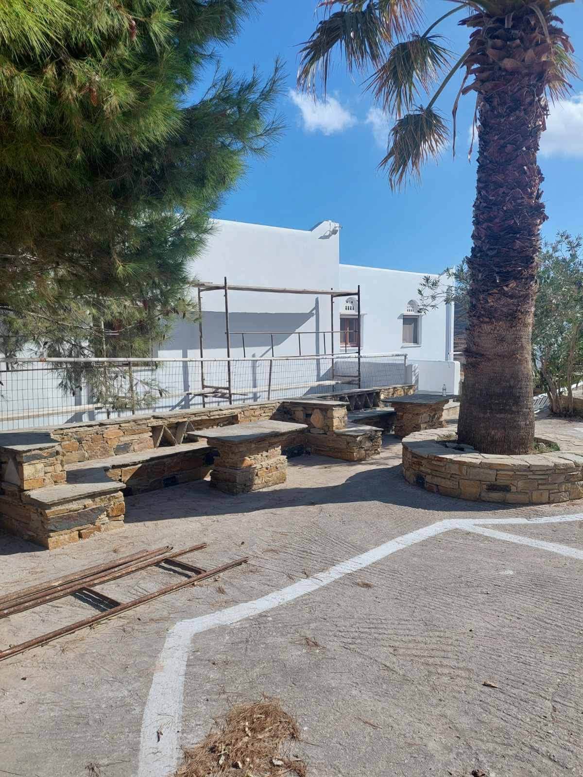 Η αυλή με τον φοίνικα και τα πέτρινα τραπέζια μπροστά στους ξενώνες