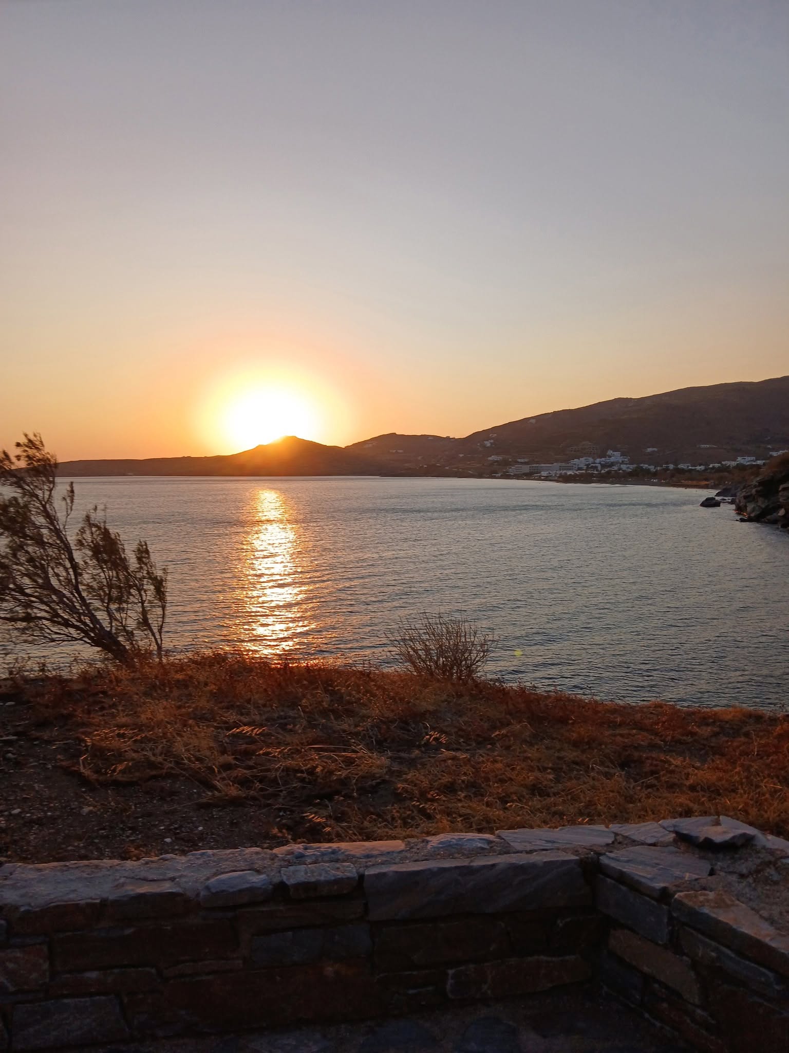 Ο ήλιος δύει πίσω από τους λόφους της Τήνου με αντανάκλαση στη θάλασσα